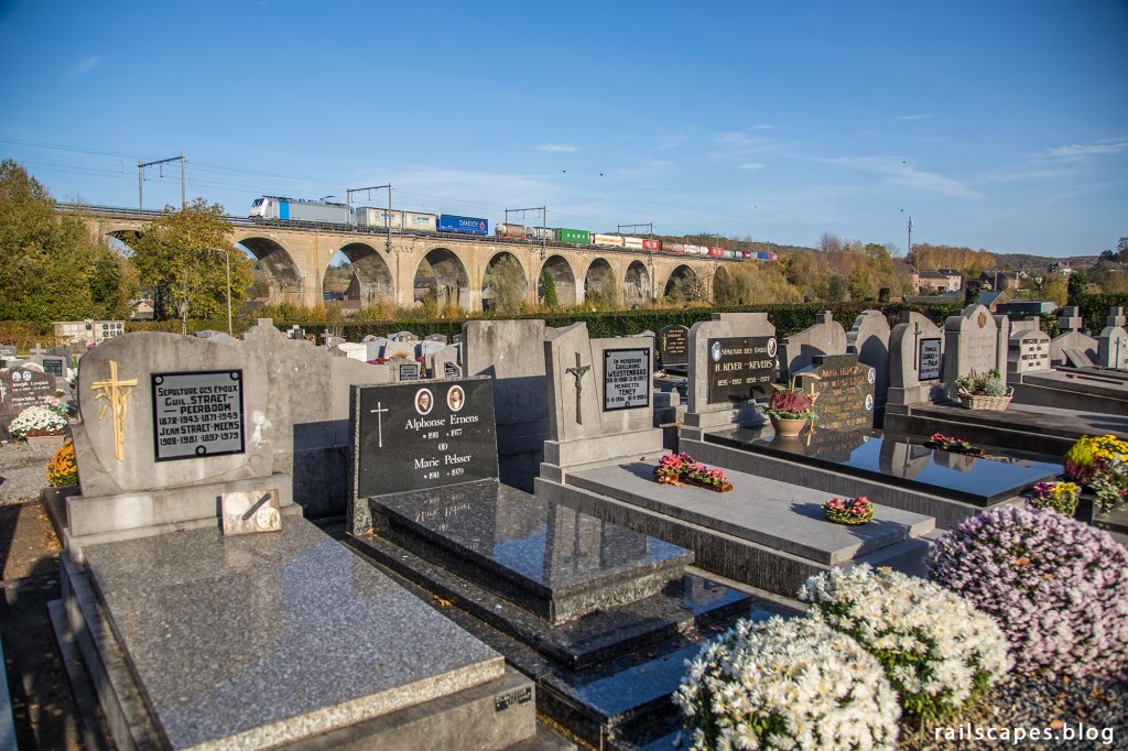 Lineas’ 186 254 leas a container train from Gallarate past Sint-Martens-Voeren’s graveyard. November 7, 2020